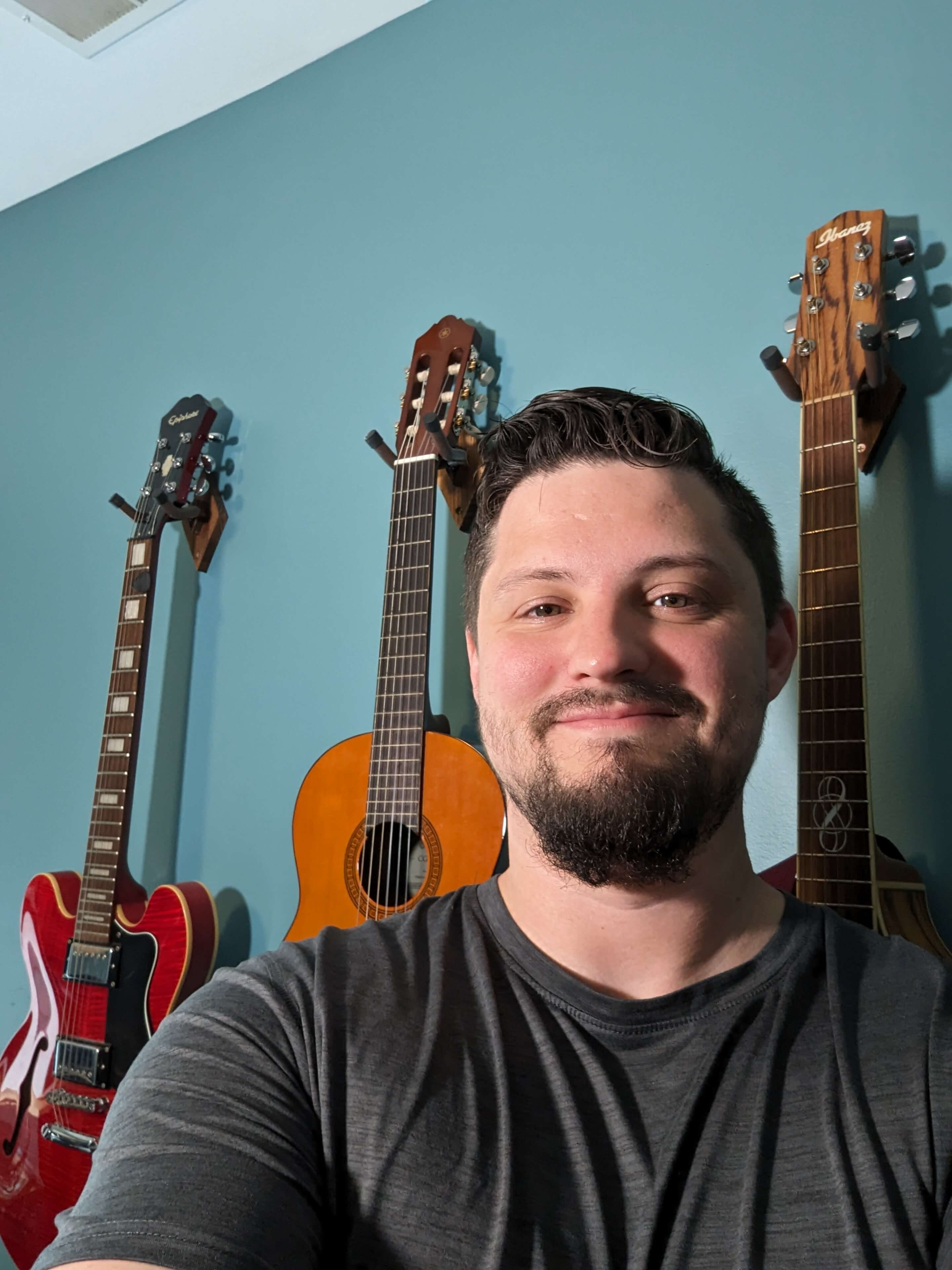 Preston Choate smiling in front of guitars on a blue wall